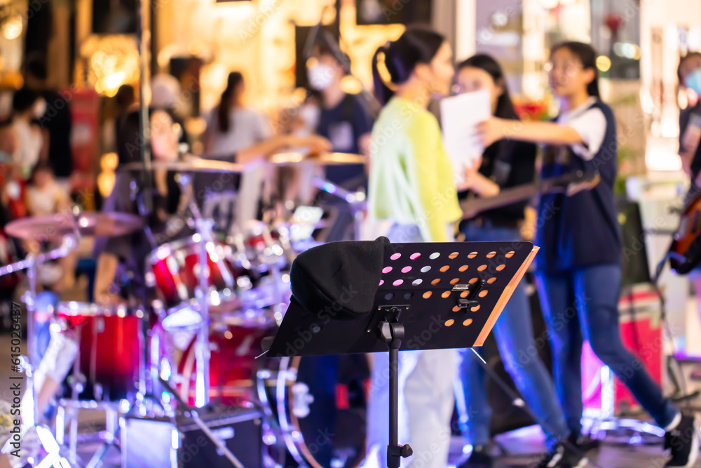 Selective focus to black music stand with blurry girl group music band and concert audience. Music concert background.