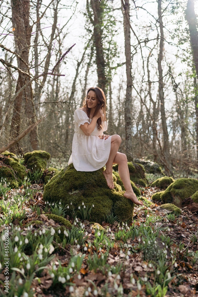 Portrait of a woman in the forest. She is sitting in a white dress on a meadow with snowdrops in a spring forest Portrait of a woman in the forest. She is sitting in a white dress on a meadow with snowdrops in a spring forest