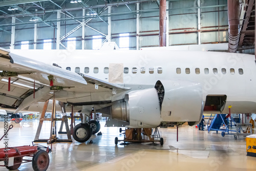 White passenger jet plane in the hangar. Jetliner under maintenance. Checking mechanical systems for flight operations