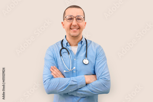 Portrait of happy male doctor with stethoscope looking at camera on beige background. Health care and medicine