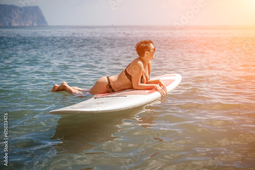 Woman sup sea travel. Sports girl on a surfboard in the sea on a sunny summer day. In a black bathing suit, he sits on a sapa in the sea. Rest on the sea. © svetograph