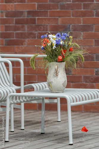 Wild flower bouquet (Cornflowers, chamomiles wheat and poppies) in terracotta vase on summer terrace. Wildflower and grass varieties.