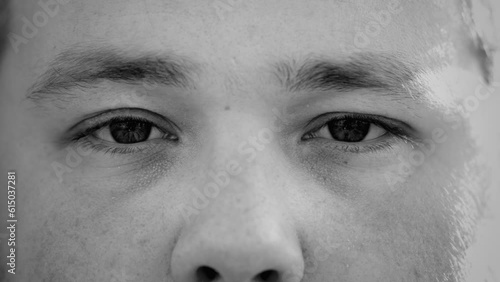 Dramatic black and white extreme macro close up of a young man staring at camera. Serious expression of a male caucasian person in monochromatic photo