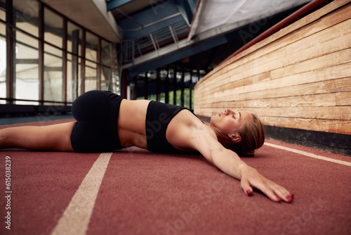 A young athlete girl is warming up before training at the stadium. A slender blonde woman in a black tracksuit does exercises to stretch her muscles while lying on a treadmill. Sports and recreation.