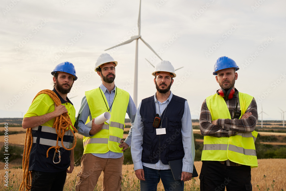 This group of colleagues work with alternative energy ,electricity, engineering and investing. It is a portrait of four engineers standing and looking at the camera outdoors in a field of windmill. This group of colleagues work with alternative energy ,electricity, engineering and investing. It is a portrait of four engineers standing and looking at the camera outdoors in a field of windmill.