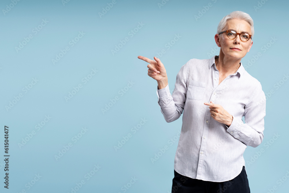 Attractive senior woman wearing glasses and casual clothes pointing fingers on copy space isolated on blue background Attractive senior woman wearing glasses and casual clothes pointing fingers on copy space isolated on blue background