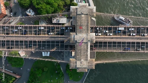Top down aerial of Brooklyn Bridge. American flag waving on top of tall suspension truss. Traffic entering Brooklyn from Manhattan, New York City.