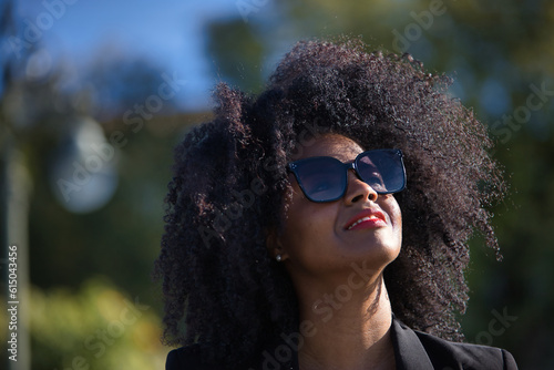 Portrait of young, beautiful, black woman with afro hair, with jacket and sunglasses, looking at the sky, grateful, praying. Concept gratitude, praying, current, modern.