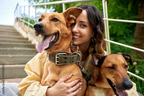 Photography Young charming smiling girl is resting while walking in the park with two golden dogs