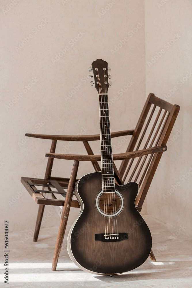 Fototapeta premium Guitar. Guitar chords. Acoustic guitar. Music. Musical background. An image of an acoustic guitar in a room with a retro armchair. Hard light. Shadows.