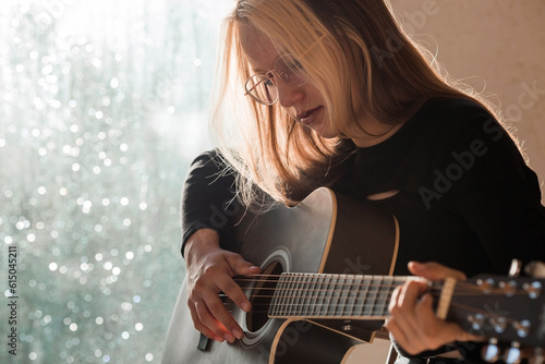 Music and hobbies. A talented young musician girl sits alone and composes songs on the guitar. The girl plays a calm melody on a musical instrument.