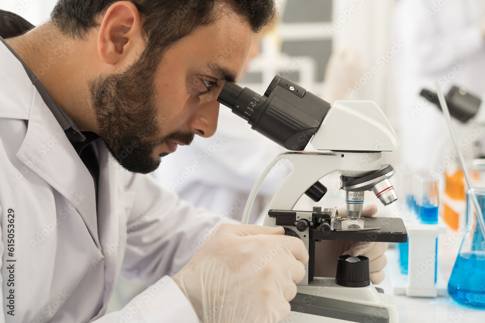 Male scientist looking through microscope doing analysis and test sample in the laboratory Male scientist looking through microscope doing analysis and test sample in the laboratory
