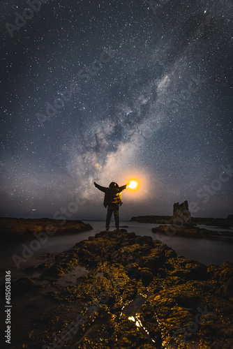 Night time long exposure landscape photography. A man standing in a high place looking up in wonder to the Milky Way galaxy, photo composite..