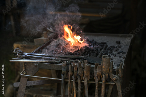 Portable forge of a blacksmith with various rusty tongs and a flaming coal fire at a historic craft market, copy space, selected focus