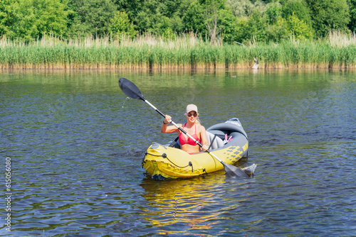A girl in a swimsuit floats on a rubber kayak on the Pirita river on a summer day, front view.
