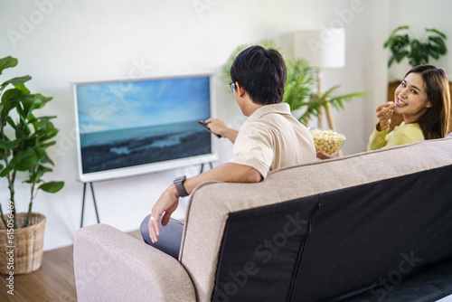 Asian family Watching smart TV together and using remote controller Hand holding popcorn at home with the remote control movie or TV series spending time at home © Charlie's