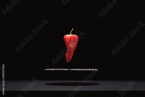 Fototapete Pimiento piquillo rojo fresco suspendido sobre un plato de pizarra y fondo negro
