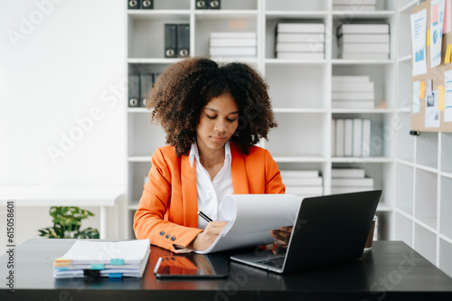 Young African woman typing on tablet and laptop while sitting at the working black table office..