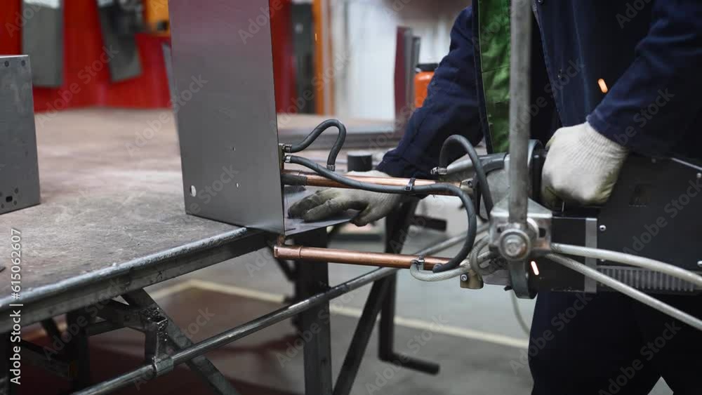 The worker at the plant is spot welding metal parts. He is using specialized, modern equipment for spot welding The worker at the plant is spot welding metal parts. He is using specialized, modern equipment for spot welding