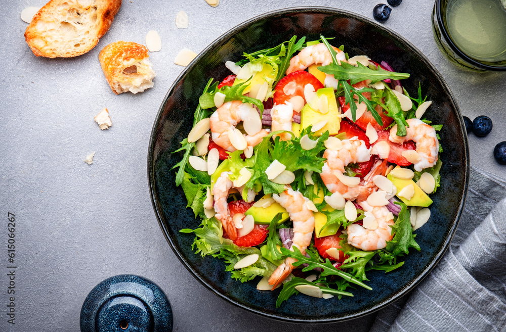 Strawberry, shrimp and herbs salad with arugula, lettuce, avocado and almond slices, gray table. Fresh useful dish for healthy eating. Top view