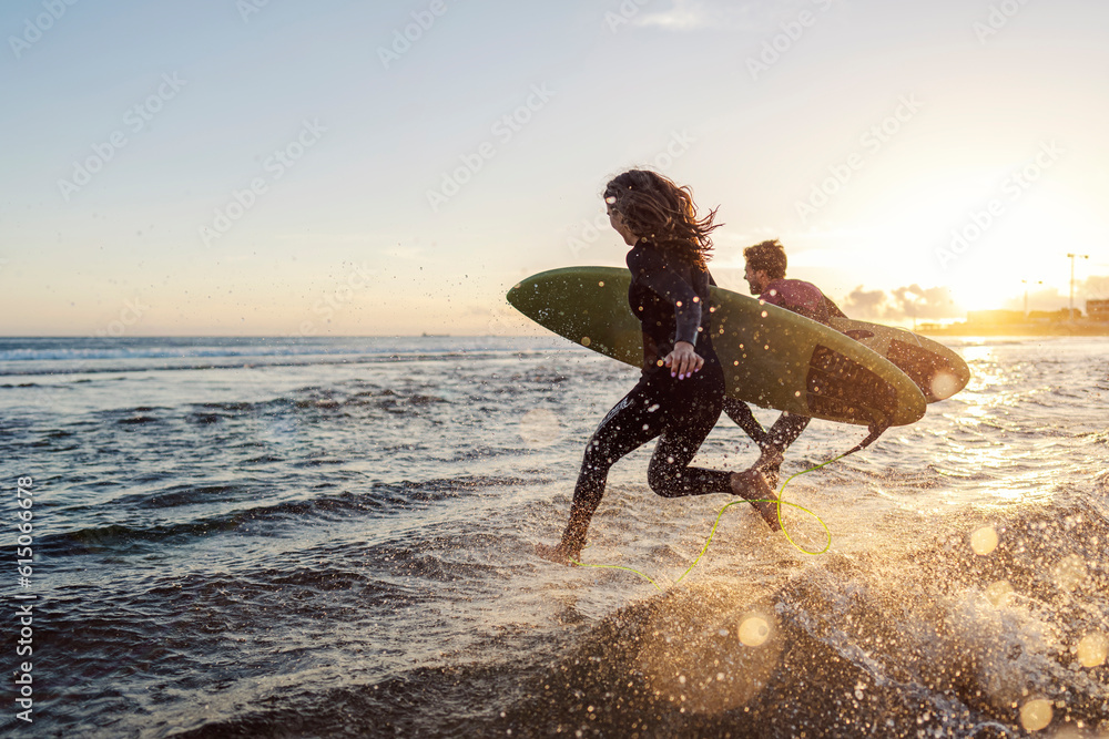 Couple is running into the water with surfboards. - obrazy, fototapety, plakaty 