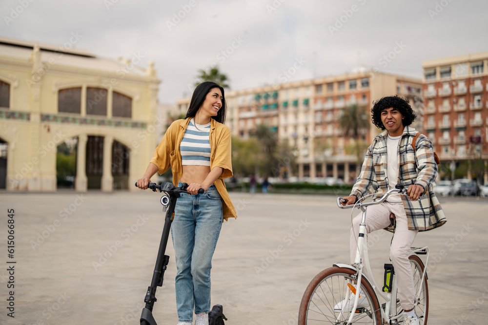 Two cheerful friends are riding a bicycle and an electric scooter and going sightseeing.