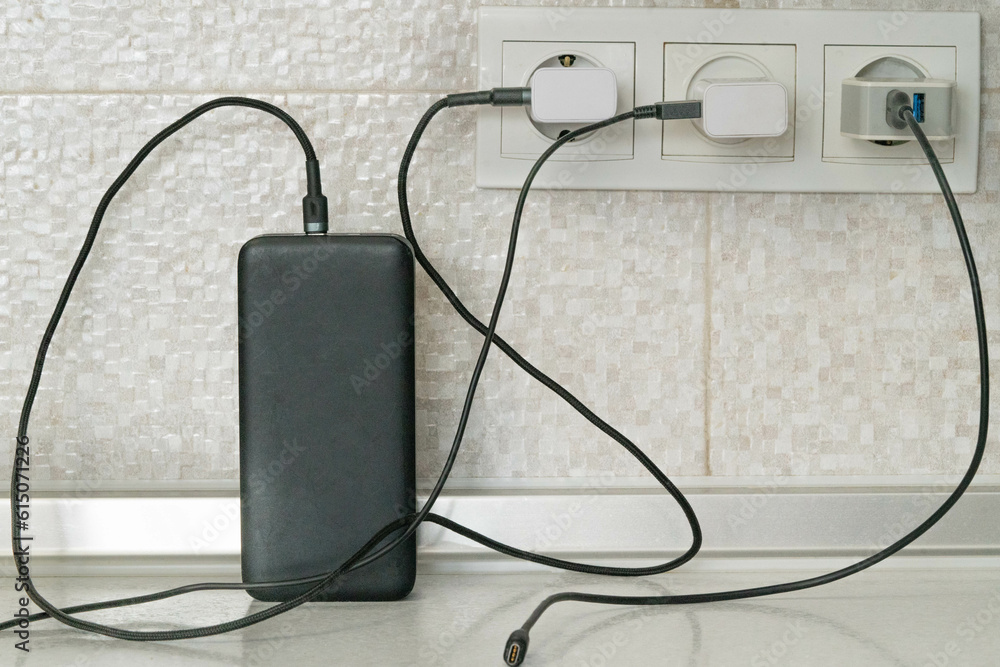 Three cables for charging electrical devices are plugged into electrical outlets, one of them charges the power bank Three cables for charging electrical devices are plugged into electrical outlets, one of them charges the power bank