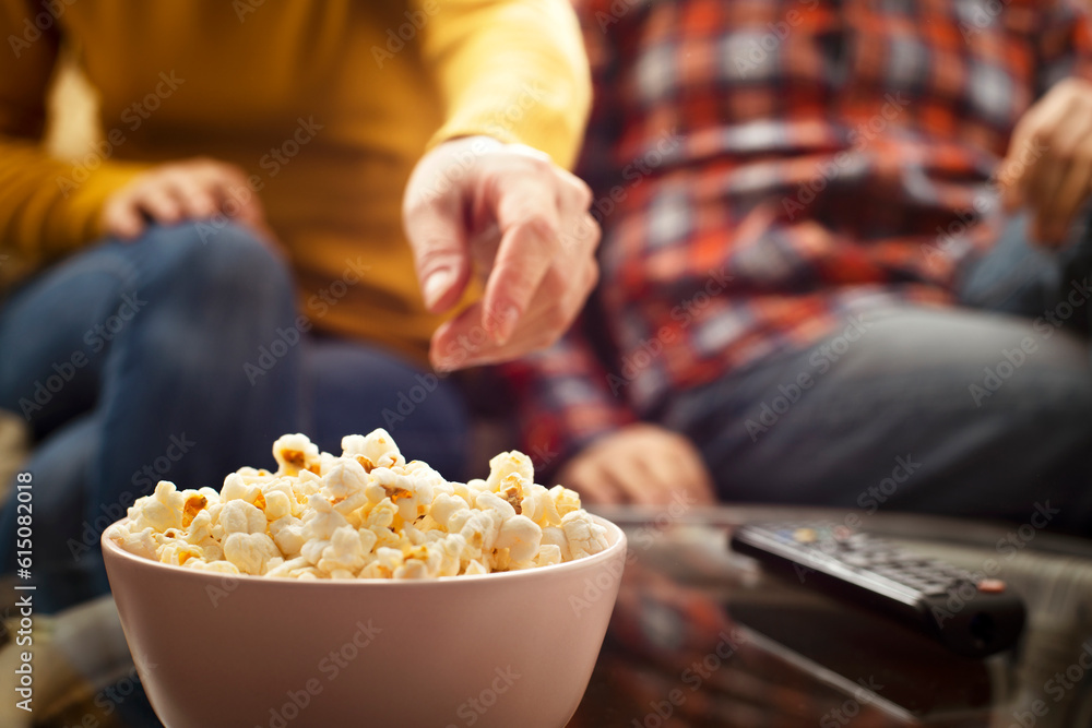 Caucasian couple sitting on sofa with popcorn and tv remote Caucasian couple sitting on sofa with popcorn and tv remote