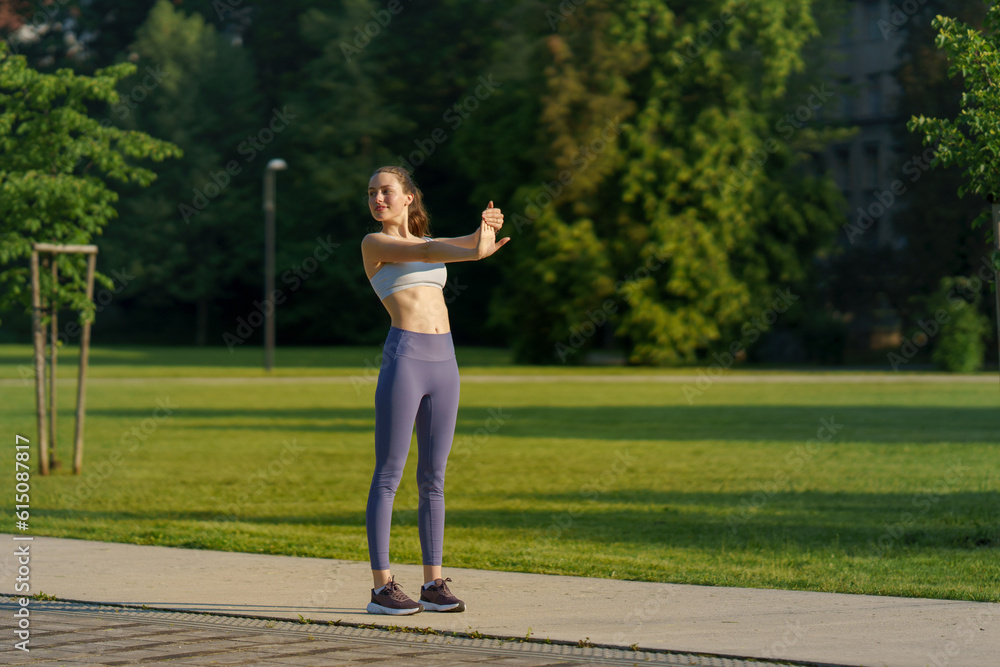 Full lenght portrait of beautiful fitness woman stretching before outdoor workout in the city park.