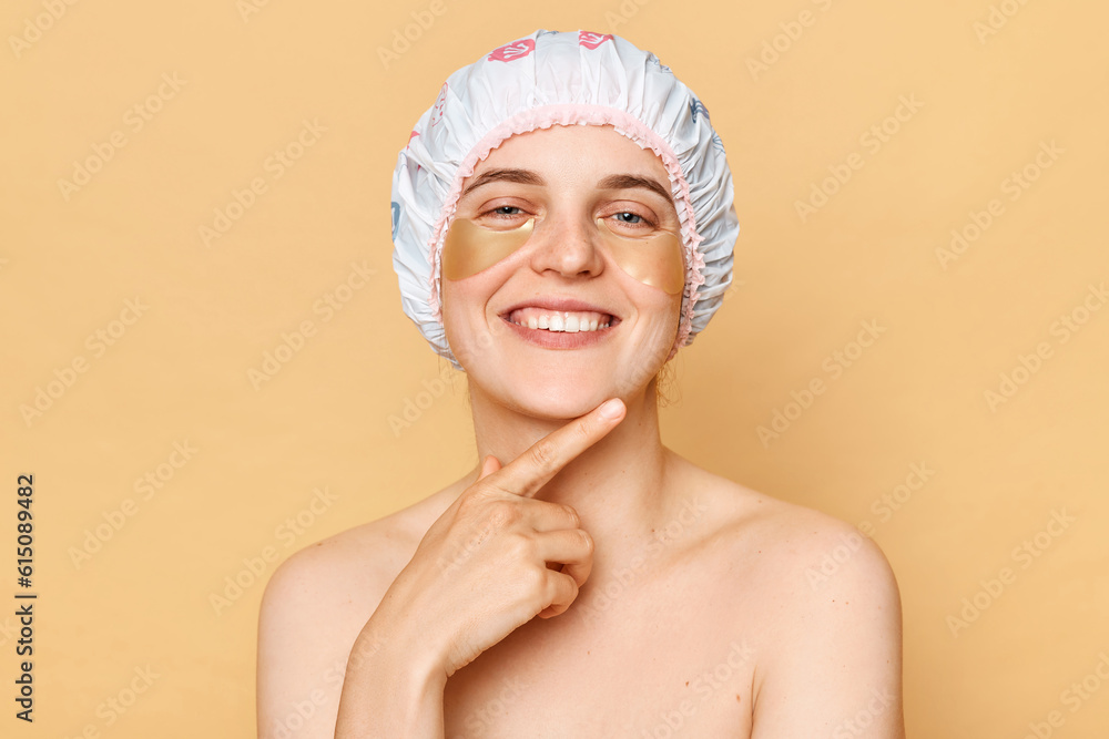 Perfect beauty regimen. Cosmetology expertise. Beauty patch application. Charming joyful woman wearing shower cap with eye patches isolated over beige background Perfect beauty regimen. Cosmetology expertise. Beauty patch application. Charming joyful woman wearing shower cap with eye patches isolated over beige background