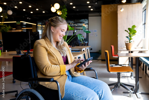 Happy plus size caucasian casual businesswoman in wheelchair using tablet in office