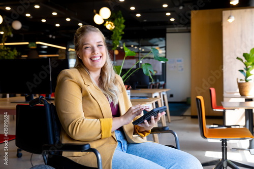 Portrait of happy plus size caucasian casual businesswoman in wheelchair using tablet in office