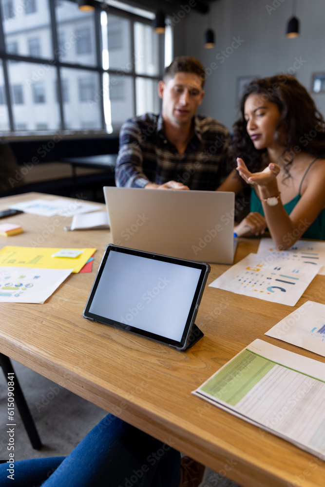 Tablet with copy space on screen and diverse colleagues in discussion at desk in casual office Tablet with copy space on screen and diverse colleagues in discussion at desk in casual office