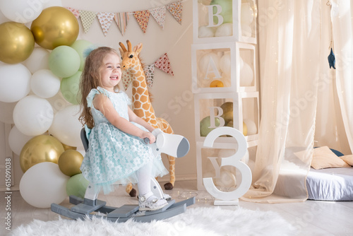 Canvas Print little girl riding a toy wooden rocking horse at home at her birthday party