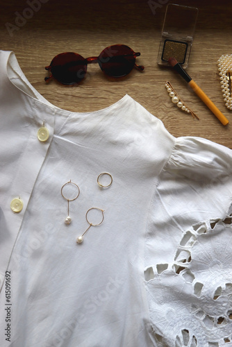 White lace blouse, straw hat, vintage bag and various accessories on wooden background. Summer outfit, flat lay.