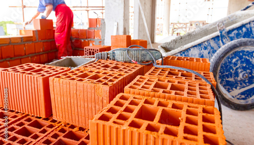 Electric drill tool on pile of red blocks, worker builds wall with bricks and mortar, building site photo