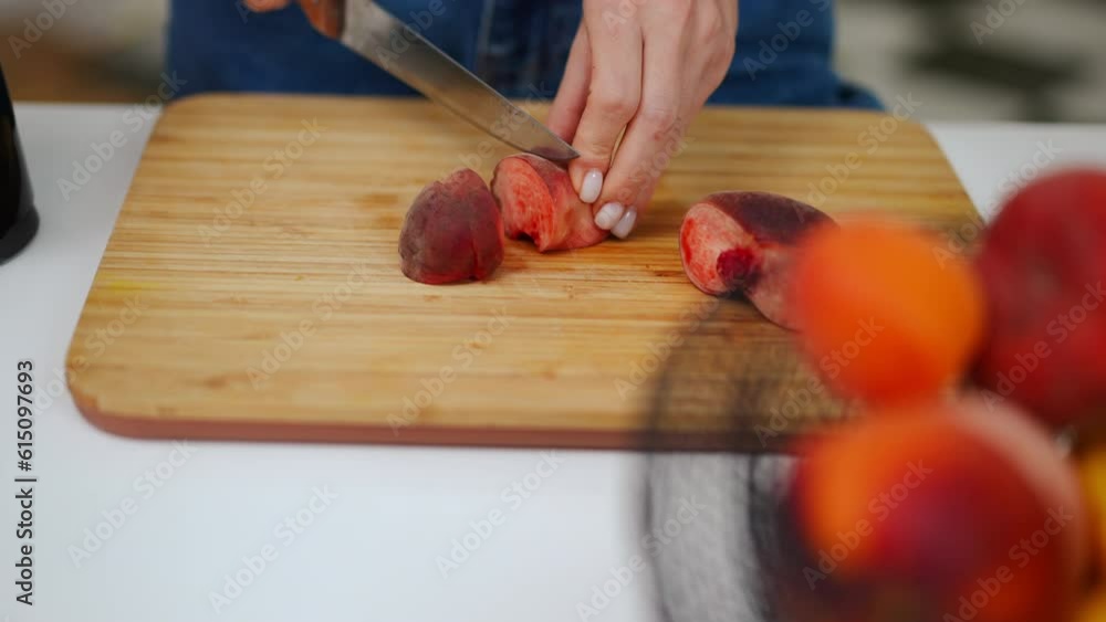 High angle view female Caucasian hands cutting flat peach on wooden board. Close-up unrecognizable young woman slicing delicious fruit in kitchen at home High angle view female Caucasian hands cutting flat peach on wooden board. Close-up unrecognizable young woman slicing delicious fruit in kitchen at home