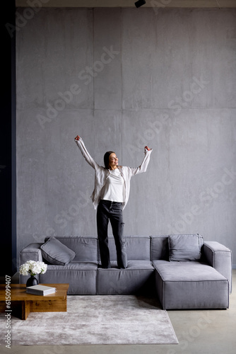 Young joyful woman in casual clothing and glasses dancing on couch in living room