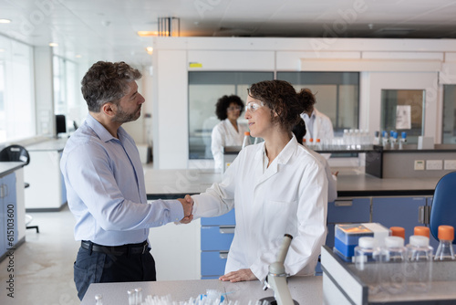 Scientist shaking hands with businessman in pharmaceutical laboratory photo