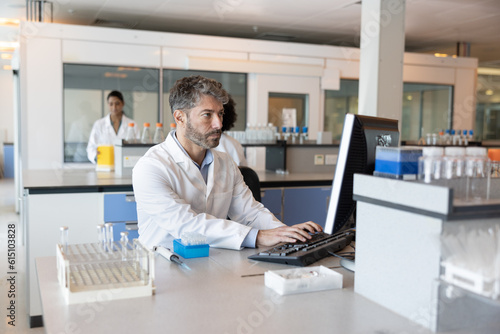 Male scientist studying data on a computer in a busy laboratory