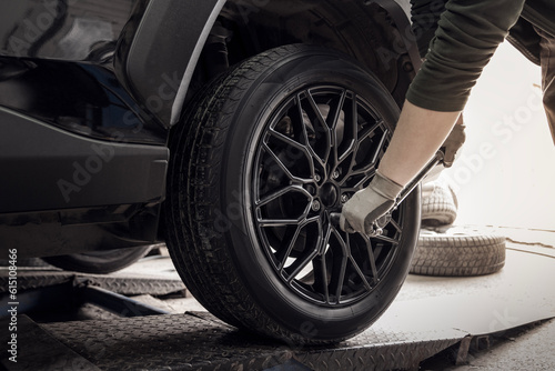 Fotografie A master tire fitter screws a new black wheel to a car in a tire service, close-