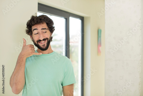 young crazy bearded man smiling cheerfully and pointing to camera while making a call you later gesture, talking on phone