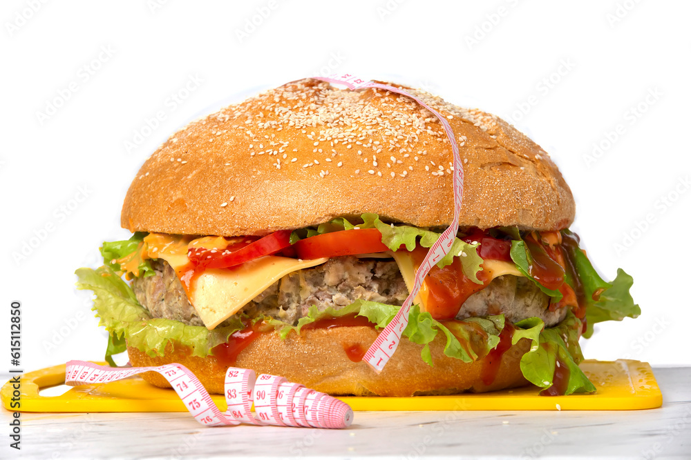 Hamburger wrapped in a measuring tape on a white background. Weight loss concept. Hamburger wrapped in a measuring tape on a white background. Weight loss concept.