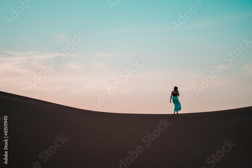 Elegant and ethereal, a woman in a blue skirt glides through a sand dune, a vision of grace amidst the textured desert backdrop