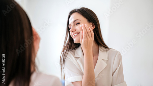 Happy female apply anti aging moisturizing cosmetic cream on face photo