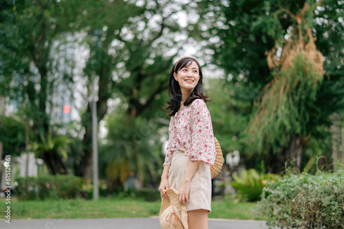 Portrait of asian young woman traveler with weaving hat and basket happy smile on green public park nature background. Journey trip lifestyle  world travel explorer or Asia summer tourism concept.