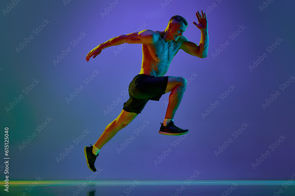 Dynamic image of young man with muscular, strong, fit body, professional runner in motion against blue studio background in neon light