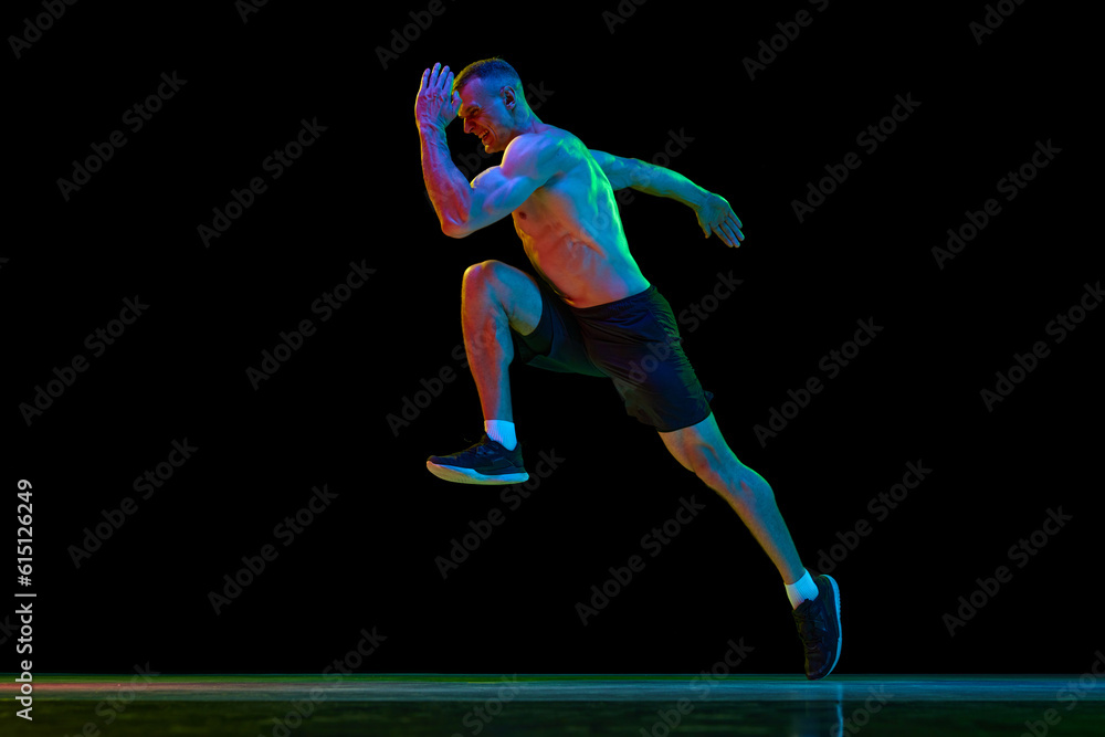 Young man with fit, muscular, relief body shape, professional sportsman in motion, running against black studio background in neon light