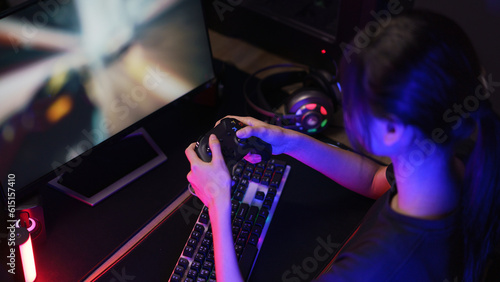 Female cyber hacker gamer playing or streaming video games on computer with joystick in neon light