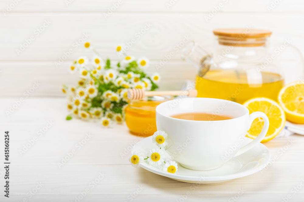 Herbal chamomile tea in a white cup on a white wooden table with honey, lemon and chamomile bouquet. Close-up. Copy space. Useful herbal drinks, immunity tea. Natural healer concept.